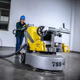 A professional operator in a hard hat pushing a large, yellow industrial floor machine for concrete grinding and polishing.