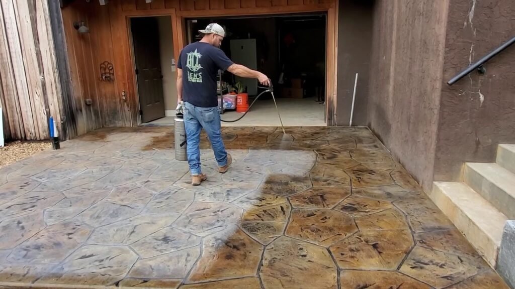 Contractor spraying brown stain during a concrete staining process on an outdoor patio