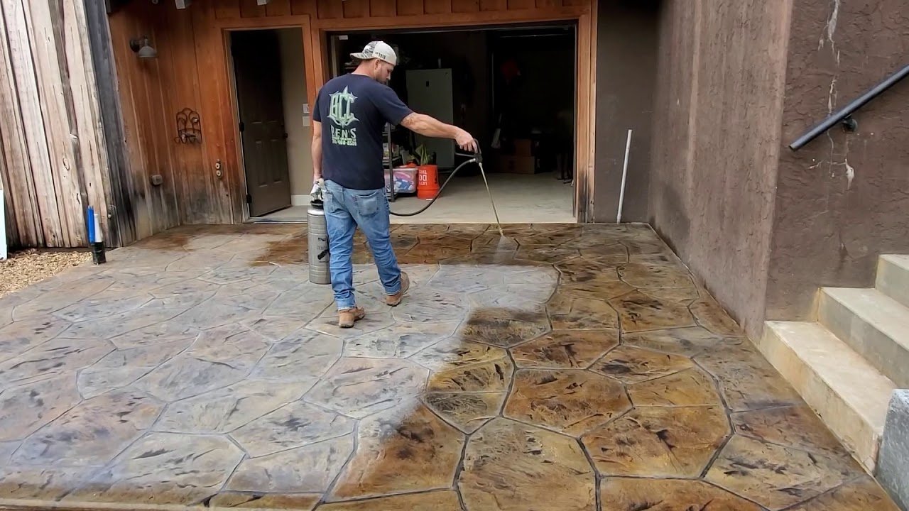 Contractor spraying brown stain during a concrete staining process on an outdoor patio